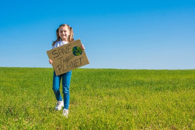 青い空と緑の野原で、地球を救うと言う段ボールの看板を持っている少女。