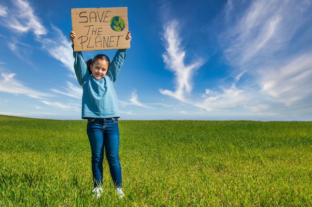 Little girl In A Green Field With A Blue Sky, Holding A Cardboard Sign That Says SAVE THE PLANET.