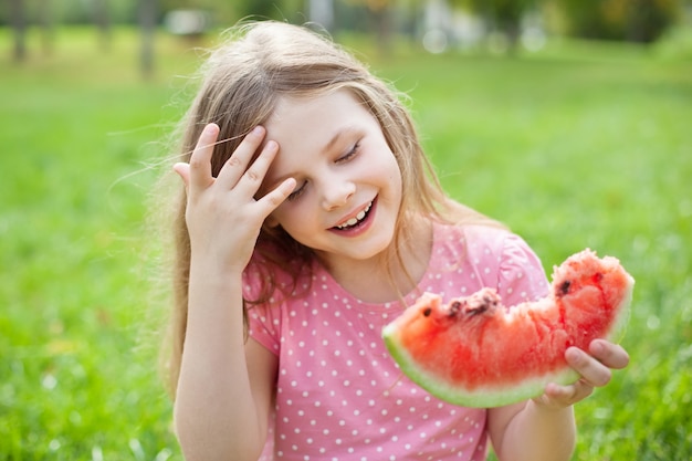 Little girl on green grass eating watermelon