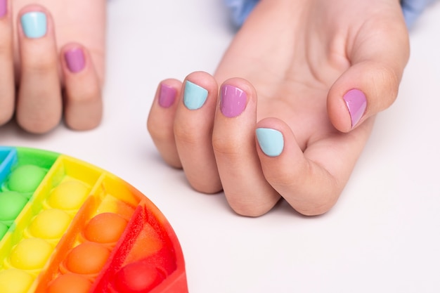 Little girl hands with beautiful manicure nails near toy pop it