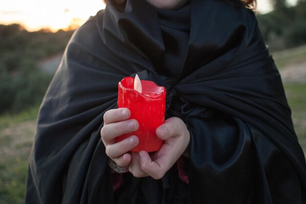 Photo little girl hands with red halloween candle and black cloak