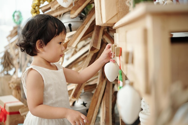 Маленькая девочка вешает безделушку на ручку шкафчика при украшении квартиры на рождество