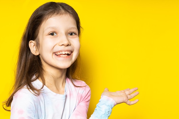 Piccola ragazza. felicità. il bambino felice mostra con la sua mano su uno sfondo giallo, un'infanzia felice.