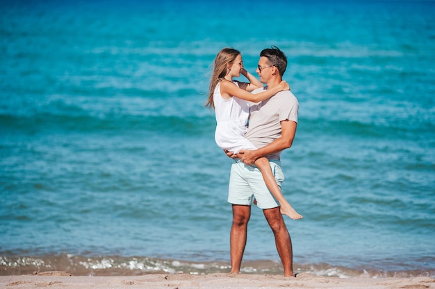 小さな女の子と幸せなお父さんがビーチでの休暇中に楽しんでいます