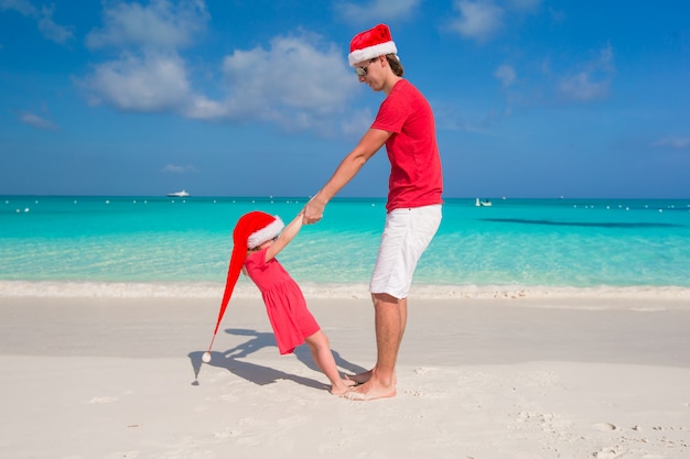 산타 모자에 어린 소녀와 행복한 아빠는 열대 해변에서 재미를