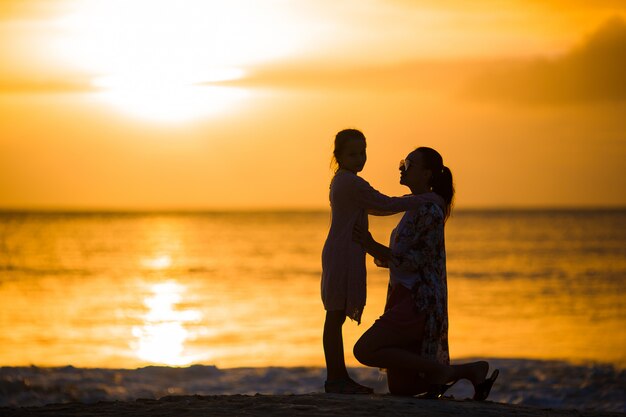 Little girl and happy mother silhouette in the sunset at the beach