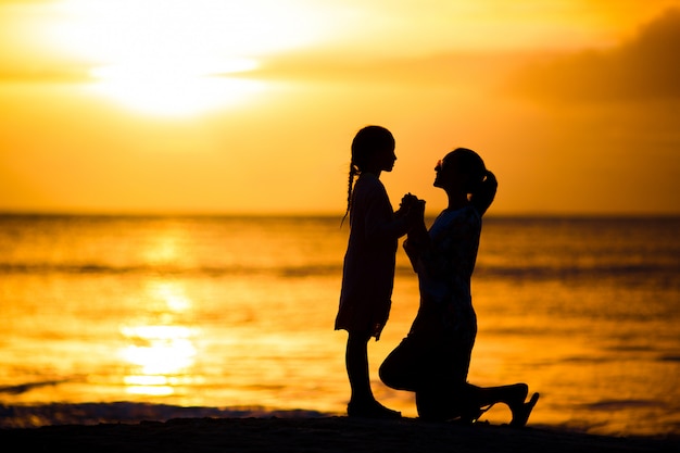 ビーチで夕日に小さな女の子と幸せな母のシルエット