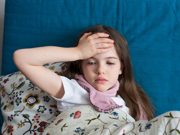 A little girl has flu, lies at home under a blanket, her head hurts