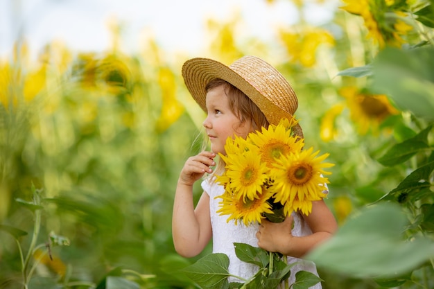 A little girl in a hat holds a bouquet of sunflowers in a field of sunflowers