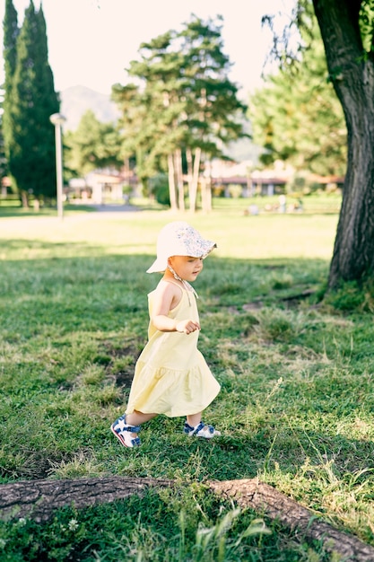 Little girl in a hat walks between trees in the park