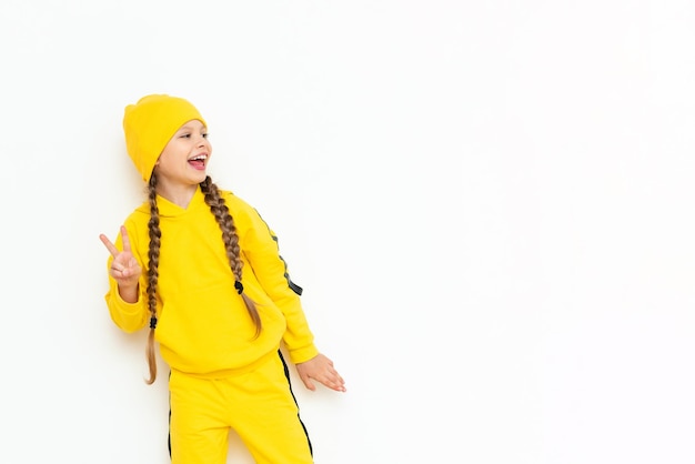 Una bambina con un cappello e un vestito giallo indica il tuo annuncio su uno sfondo bianco isolato abiti autunnali per bambini copia spazio