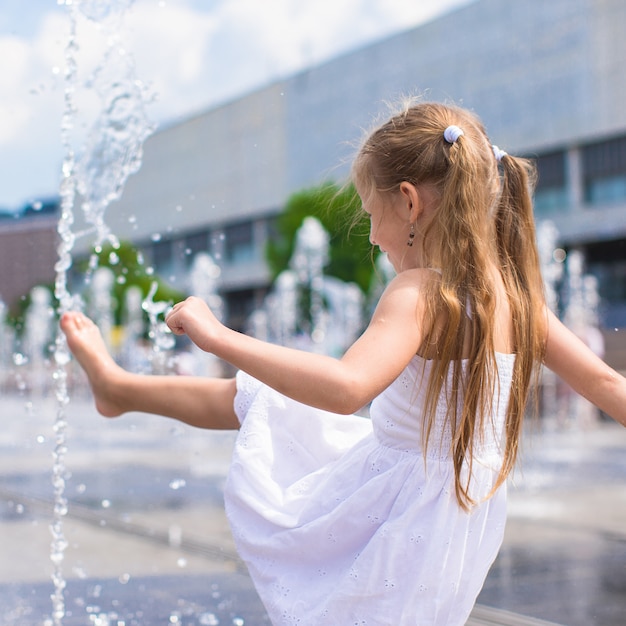 小さな女の子は、暑い夏の日に開かれた通りの噴水で楽しい時を過す