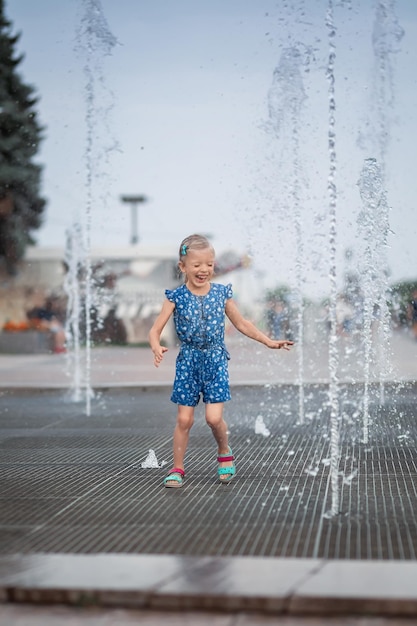 Little girl having fun in fountains hot summer weather in city\
little girl running near fountains in hot weather child running\
between water jets of fountains