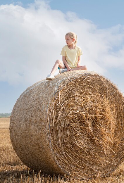 Little girl having fun in a wheat field on a summer day. Child playing at hay bale field during harvest time.