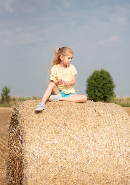 Маленькая девочка с удовольствием на пшеничном поле в летний день. Ребенок играет на поле тюков сена во время сбора урожая.