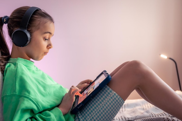 a little girl in headphones plays a game on a tablet
