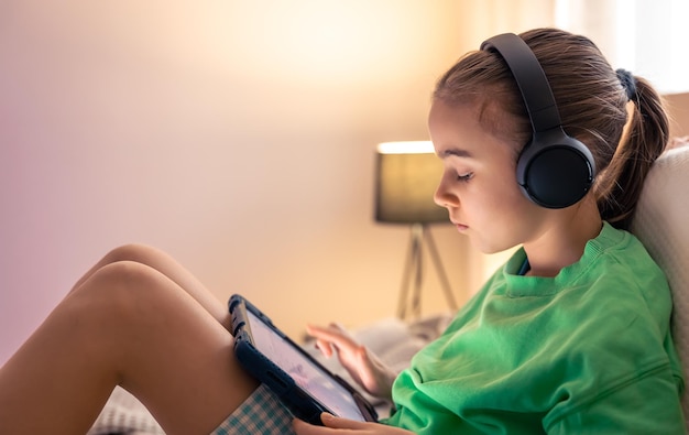 little girl in headphones with a tablet in her room