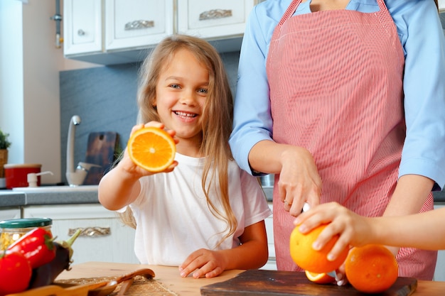 Little girl helping her mom to cut oranges