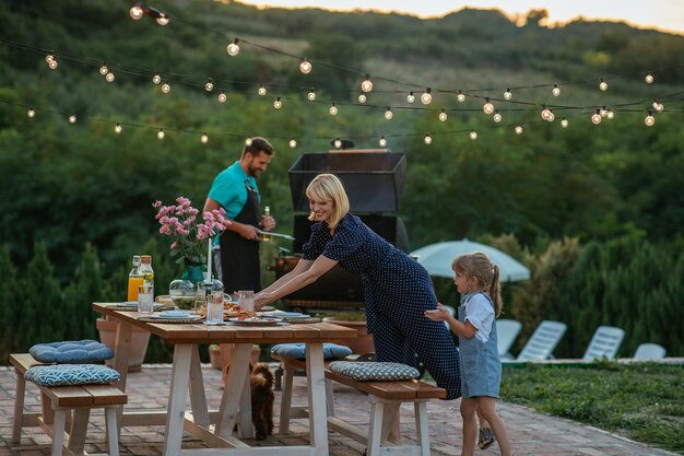 Photo little girl helping mother to arrange dining table in the backyard