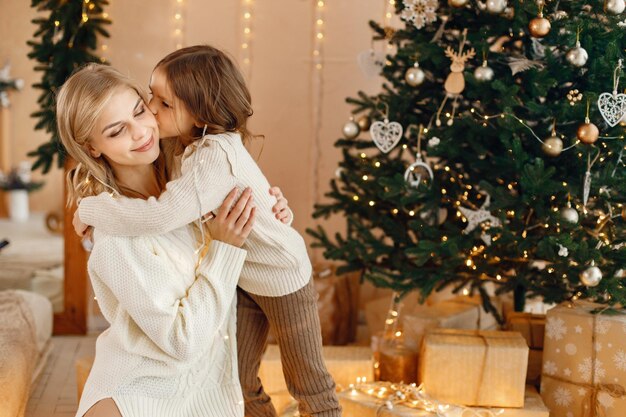 Little girl and her mom sitting near Christmas tree and hugging