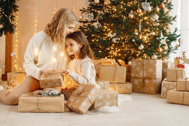 Little girl and her mom sitting near Christmas tree with gift box