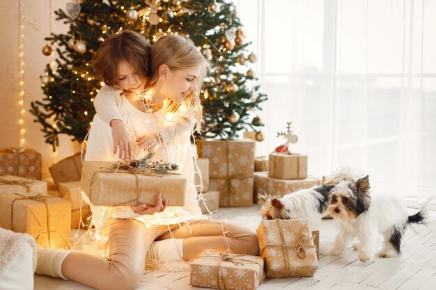 Little girl and her mom sitting near Christmas tree with yorkshire terriers