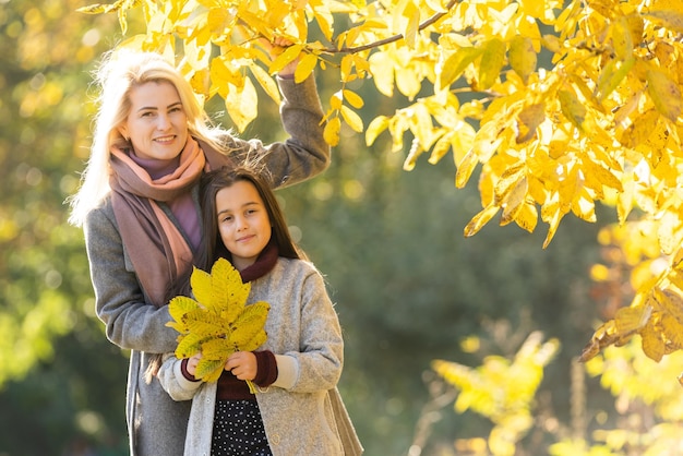 Little girl and her mother enjoy sunny weather in the autumn park.