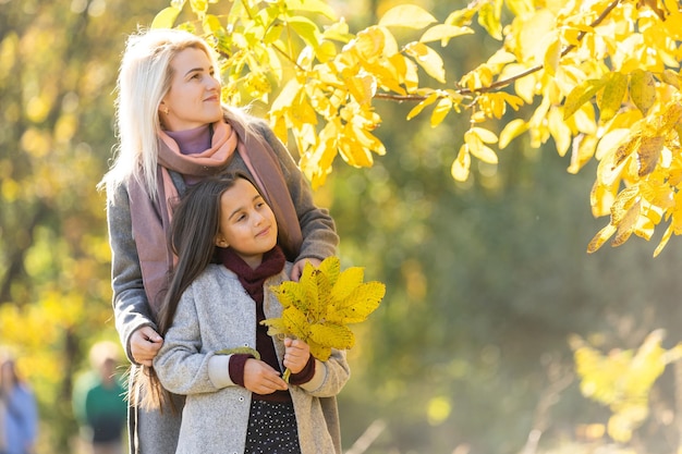 Little girl and her mother enjoy sunny weather in the autumn park.