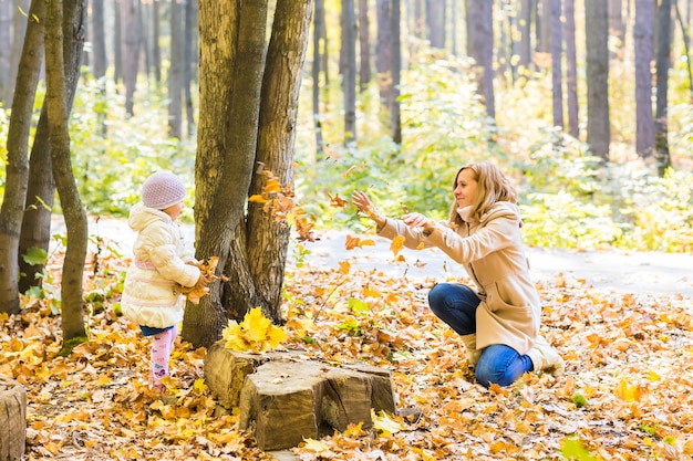 Маленькая девочка и ее мать играют в осеннем парке.
