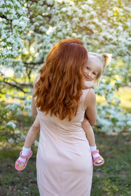 Little girl in her mother's arms against the background of a blooming garden