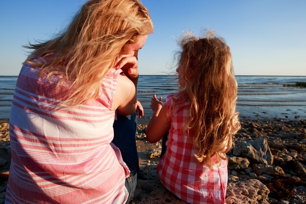 Little girl and her mother sitting on a rocky shore and looking at the sea.