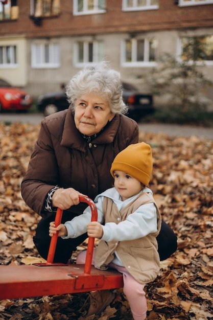 a little girl and her old grandmother are playing in the yard of the house in autumn