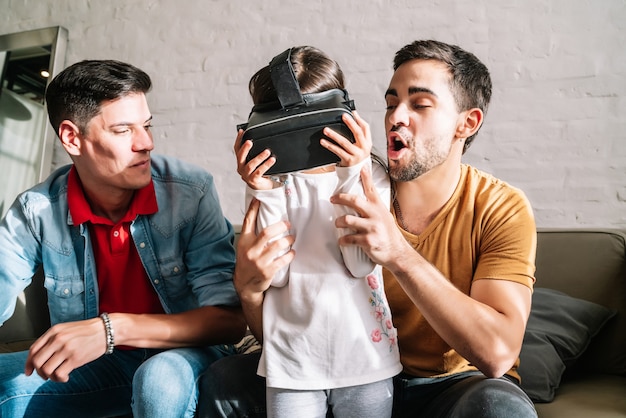 Little girl and her parents playing video games with VR glasses at home. Family concept.