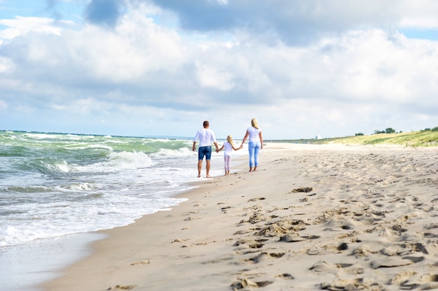 어린 소녀와 그녀의 부모는 리투아니아의 발트해 해변을 걷고 있습니다.