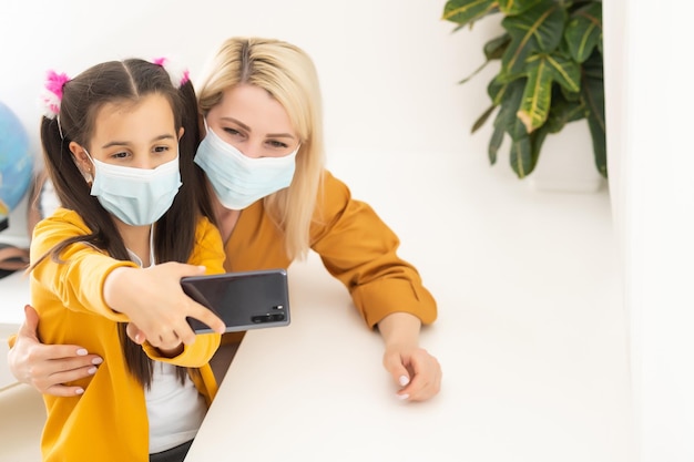 Little girl and her young mother taking a selfie wearing surgical mask.