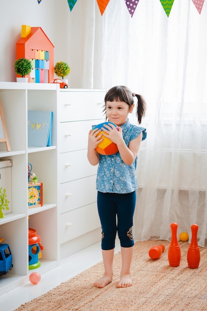 Bambina che tiene una palla nella stanza del gioco.