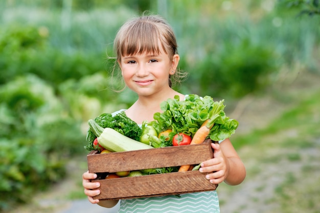 有機バイオファームで収穫有機野菜と根でいっぱいのバスケットを持っている少女。秋の野菜の収穫。