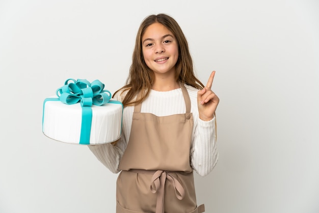 Bambina con una grande torta su sfondo bianco isolato che mostra e alzando un dito in segno del meglio