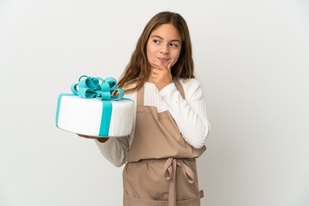 Little girl holding a big cake over isolated white wall and looking up