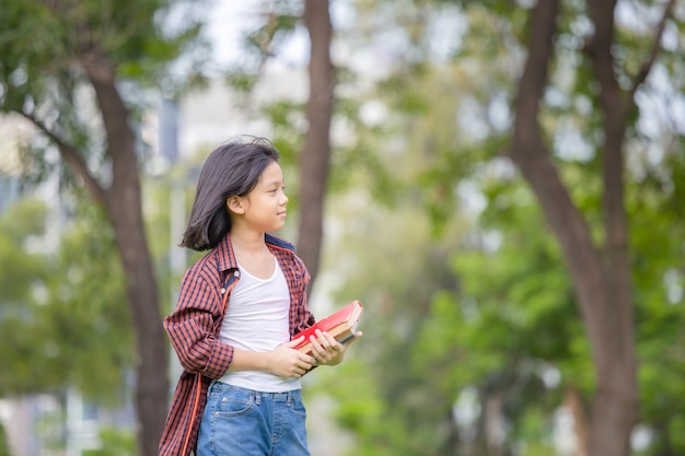 Маленькая девочка держит книгу и гуляет в парке
