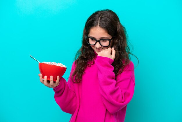 Little girl holding a bowl of cereals isolated on blue background celebrating a victory