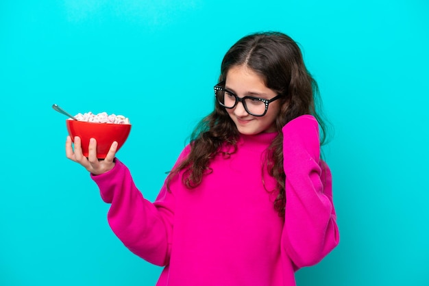 Little girl holding a bowl of cereals isolated on blue background celebrating a victory