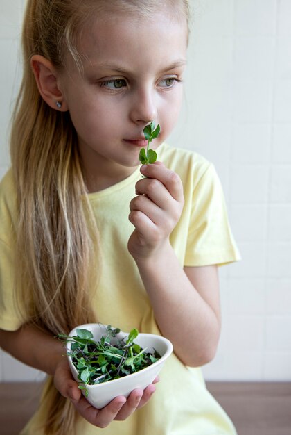 Photo little girl holding a bowl with microgreens in her hands. healthy eating concept