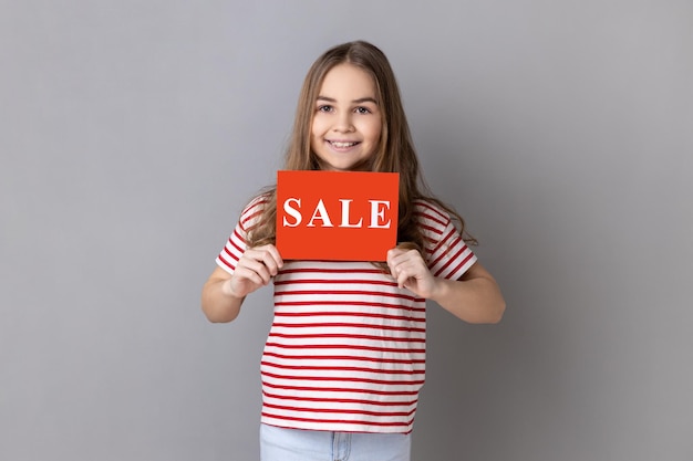 Photo little girl holding card with sale inscription looking at camera with toothy smile