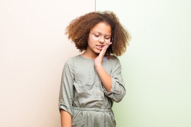 Little girl holding cheek and suffering painful toothache, feeling ill, miserable and unhappy, looking for a dentist over wall