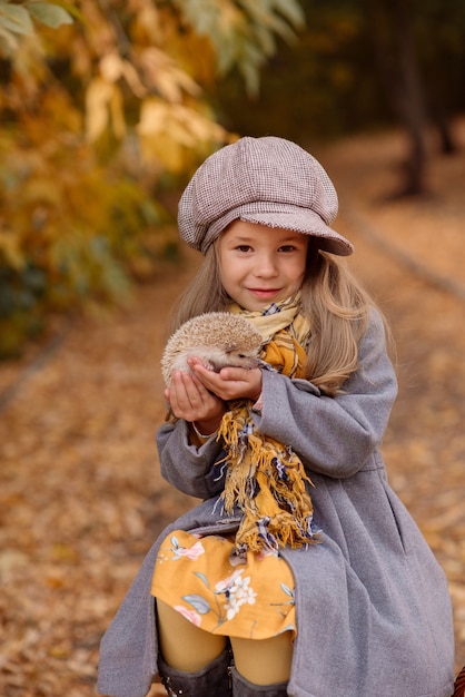 Bambina che tiene un divertente riccio tra le braccia in autunno nel parco