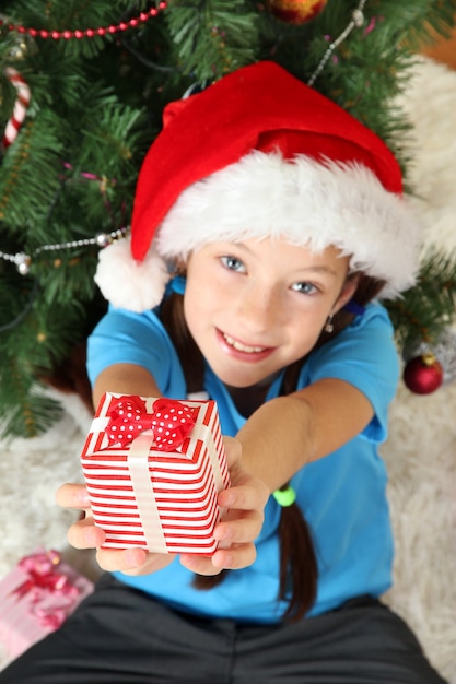 Little girl holding gift box near christmas tree