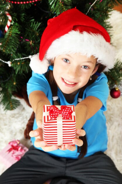 Little girl holding gift box near christmas tree