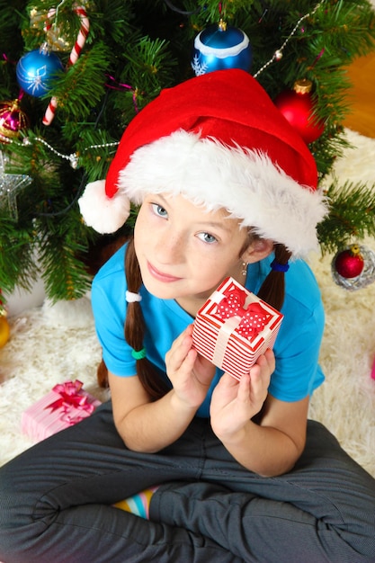 Little girl holding gift box near christmas tree