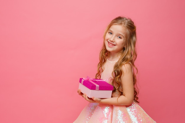 A little girl holding a gift in her hands smiles on a pink space.